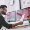 Side view of information security analyst looking at charts near graphs on computer monitors in office