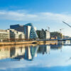 Modern buildings and offices on Liffey river in Dublin on a bright sunny day, bridge on the right is a famous Harp bridge.