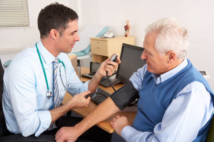 GP British doctor taking senior man's blood pressure