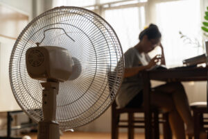 unhappy woman sitting in front of working fan suffering from heat in modern house on sunny summer day in front of working fan suffering from summer heat.