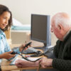 GP Young female Doctor taking senior man's blood pressure