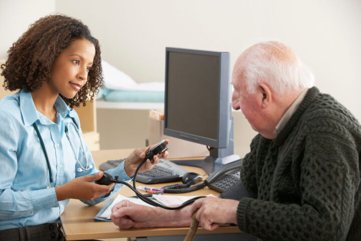 GP Young female Doctor taking senior man's blood pressure