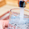 Closeup shot of a man pouring a glass of fresh water from a kitchen faucet