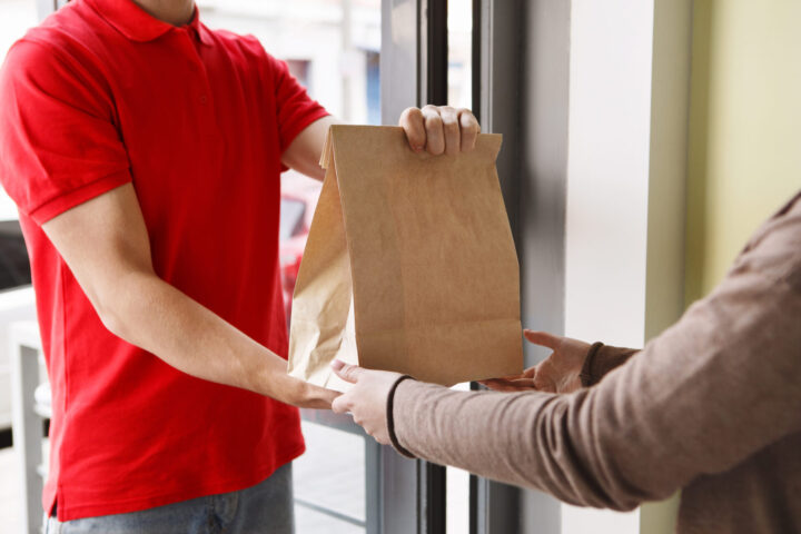 Modern delivery of any food order. Girl takes paper package from hands of courier at front door - food delivery driver