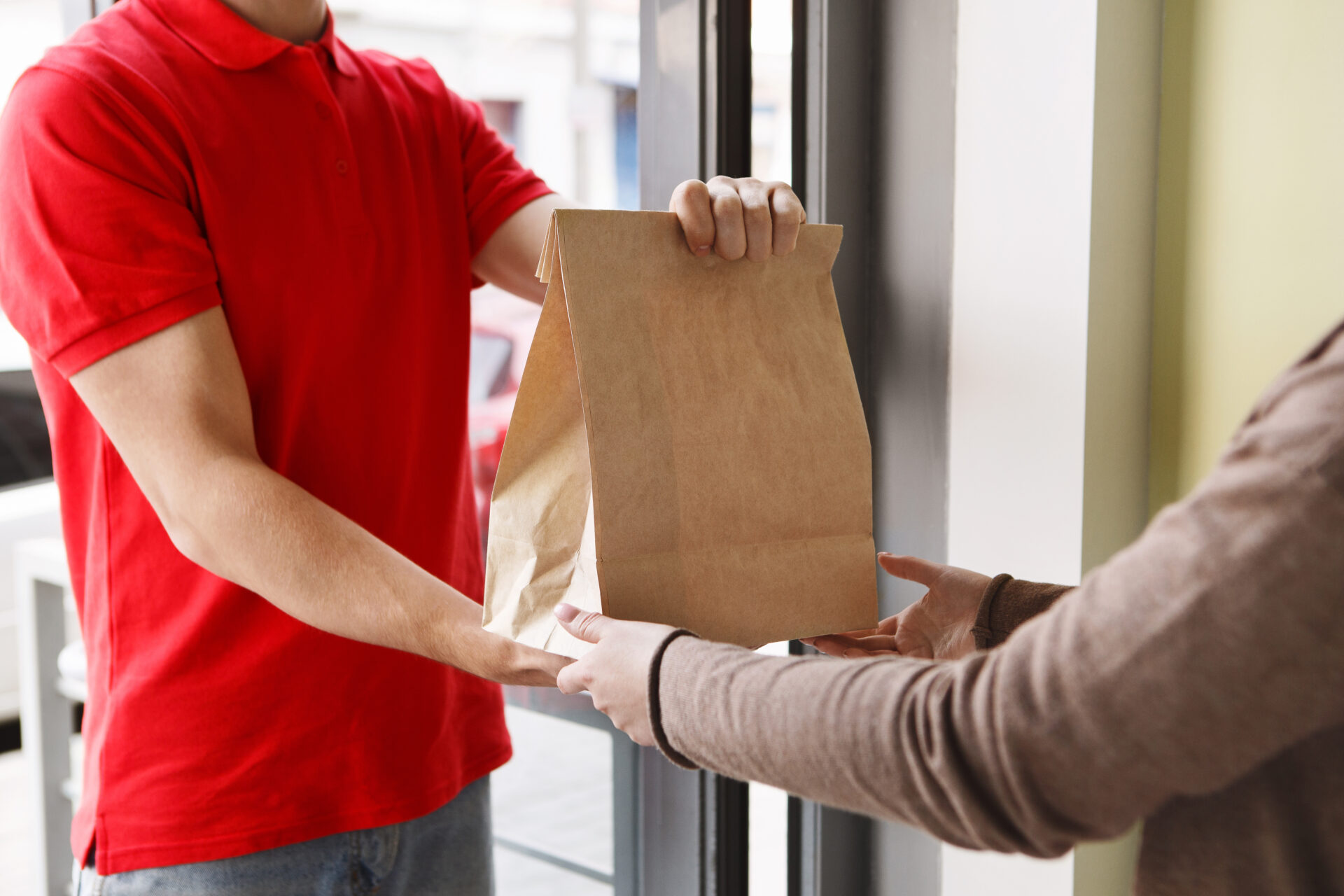 Modern delivery of any food order. Girl takes paper package from hands of courier at front door - food delivery driver