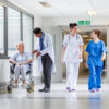 Doctors; nurse in hospital corridor with senior female patient in wheel chair with male Asian doctor NHS
