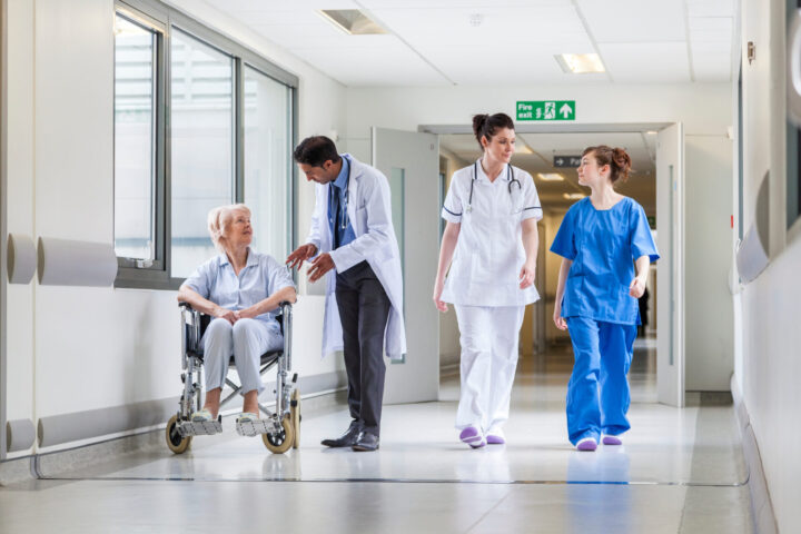 Doctors; nurse in hospital corridor with senior female patient in wheel chair with male Asian doctor NHS