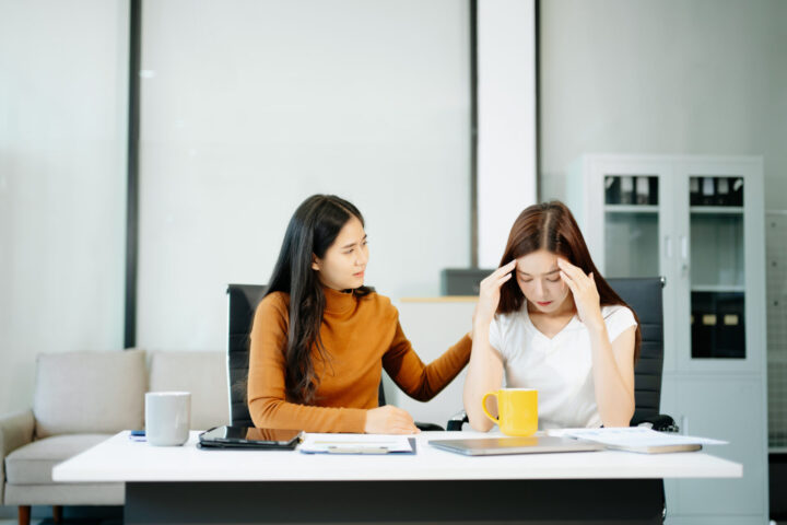 woman comforts her distressed coworker in office. Concept of workplace stress, burnout, empathy, and emotional support in professional environments.