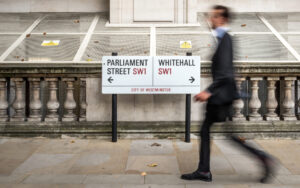Abstract anonymous blur of a suited office worker passing a street sign indicating prominent addresses of Parliament Street and Whitehall in the UK civil service district of Westminster.