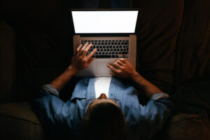 Young businessman in eyeglasses is working remotely from home late at night, looking on display, texting. Hard worker, busy man working overtime, taking work at home, has deadline. Blank screen