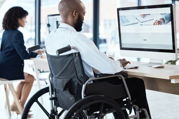 Wheelchair, office and black man disability in the workplace doing business analyst work. Working, computer and desk job of a disabled worker back planning a digital strategy for inclusive job.