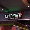 Illuminated signage for Chopstix Noodle Bar featuring the logo with crossed chopsticks. A popular Asian fast food chain restaurant entrance in a shopping mall. London, UK, 17 February 2024