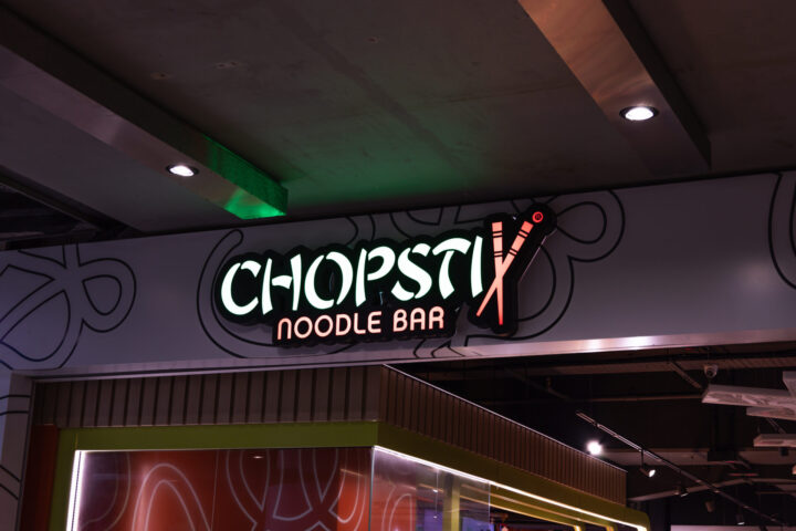 Illuminated signage for Chopstix Noodle Bar featuring the logo with crossed chopsticks. A popular Asian fast food chain restaurant entrance in a shopping mall. London, UK, 17 February 2024