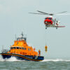 coastguard orange sea rescue boat at sea off south coast of Britain man being winched to emergency rescue helicopter