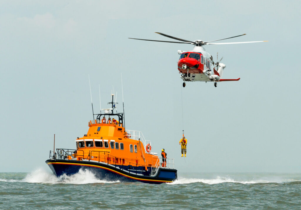 coastguard orange sea rescue boat at sea off south coast of Britain man being winched to emergency rescue helicopter