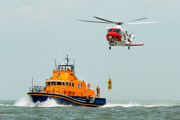 coastguard orange sea rescue boat at sea off south coast of Britain man being winched to emergency rescue helicopter