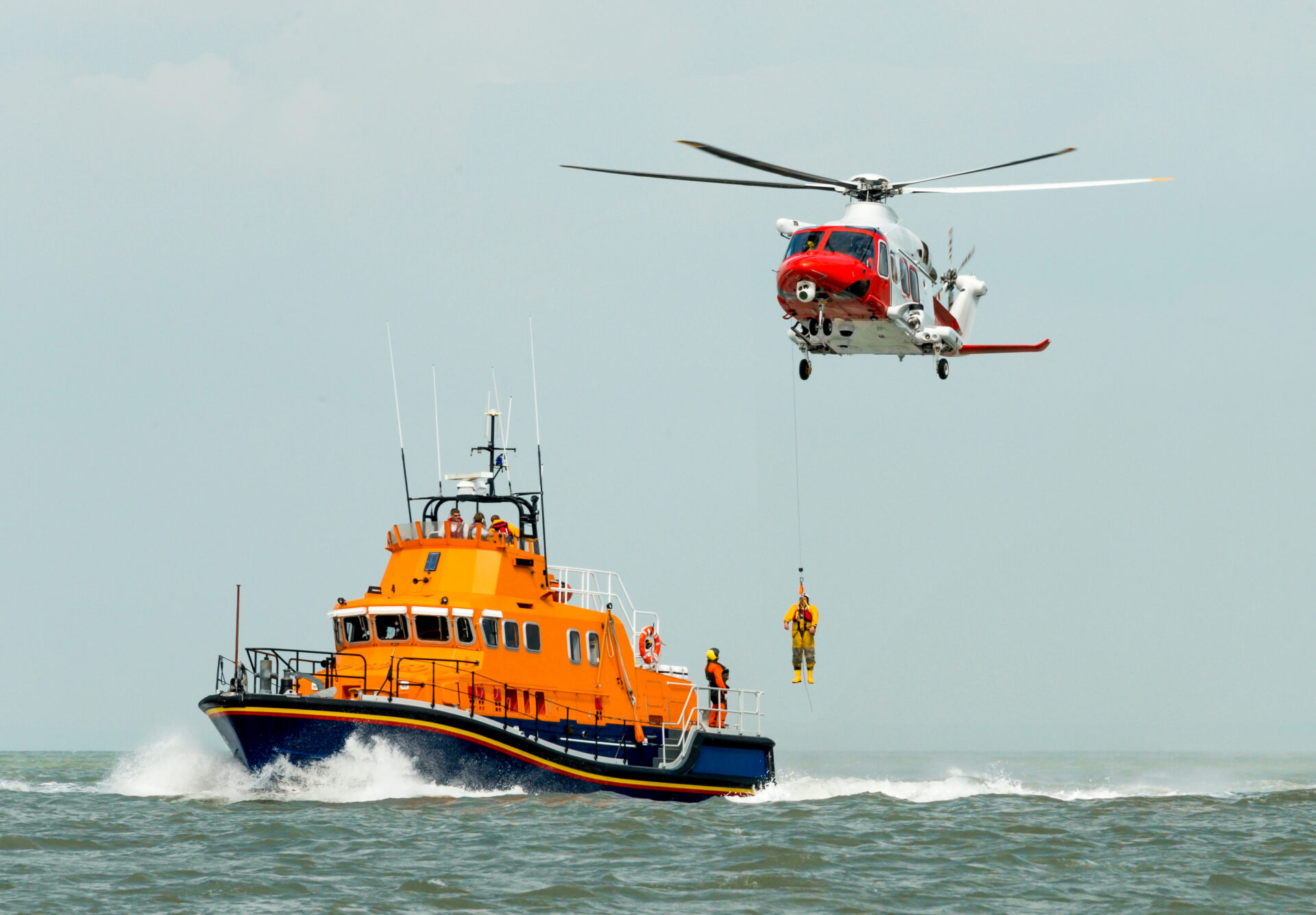 coastguard orange sea rescue boat at sea off south coast of Britain man being winched to emergency rescue helicopter