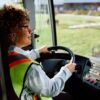 Female bus driver behind steering wheel.
