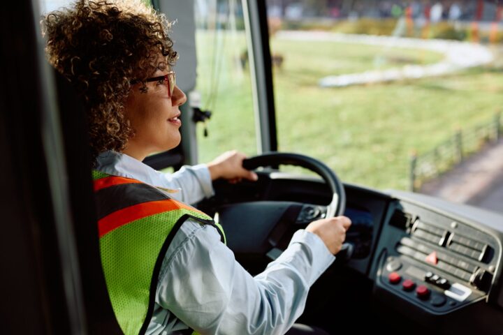 Female bus driver behind steering wheel.